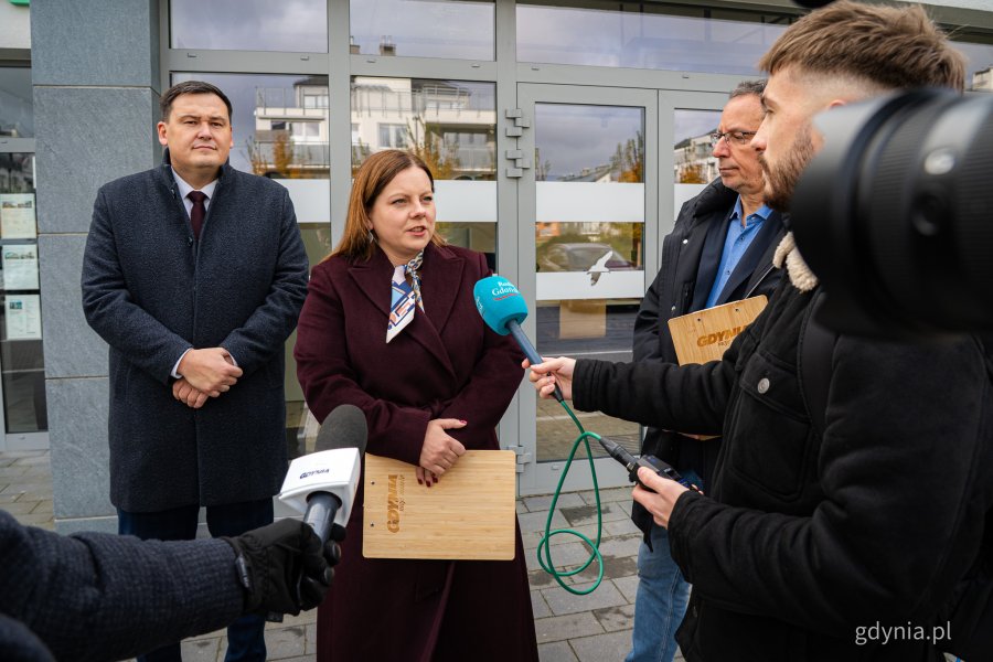 Od lewej: sekretarz miasta Łukasz Kobus, prezydent Gdyni Aleksandra Kosiorek, rzecznik prasowy Urzędu Miasta Gdyni Tomasz Złotoś i przedstawiciele mediów przed nowo otwartym Punktem Obsługi Mieszkańców Urzędu Miasta Gdyni na Chwarznie-Wiczlinie, w lokalu przy ul. Tęczowej 37 (fot. Kamil Złoch)