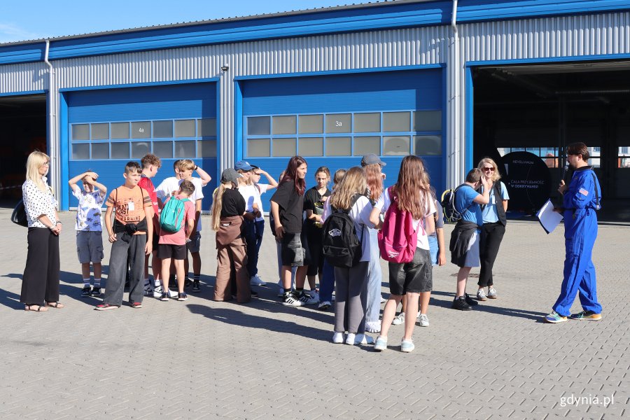 Grupa ludzi przed hangarem 