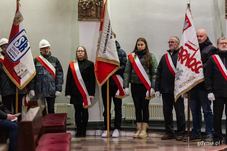 Ludzie w odświętnych strojach stoją w kościele