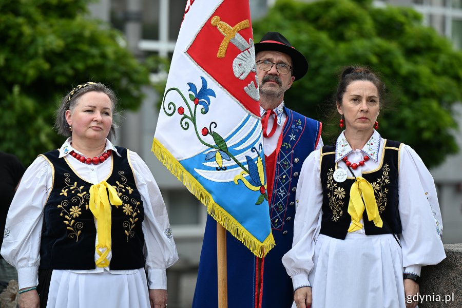 Osoby w ludowych strojach i sztandar kaszubski