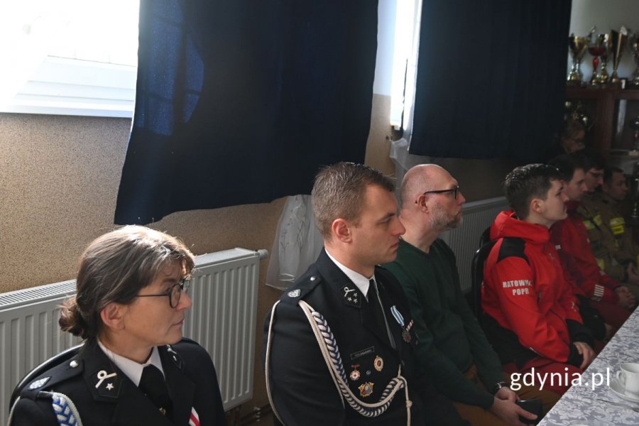 Mężczyźni i kobiety siedzący przy stole z białym obrusem i słuchający prelekcji