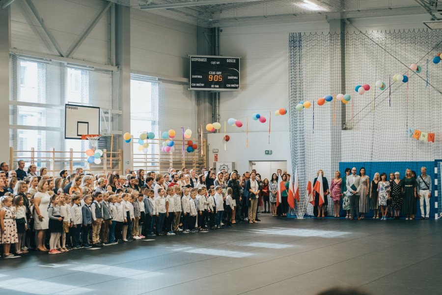 Dzieci stojące na baczność w hali sportowej śpiewające hymn Polski