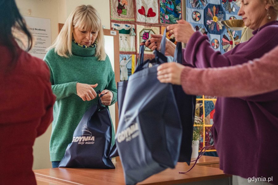 Bożena Zglińska - dyrektor Centrum Aktywności Seniora (w środku) oraz inne osoby pomagające w pakowaniu wielkanocnych paczek dla potrzebujących. Wszyscy trzymają i wiążą granatowe torby z produktami spożywczymi // fot. Kamil Złoch