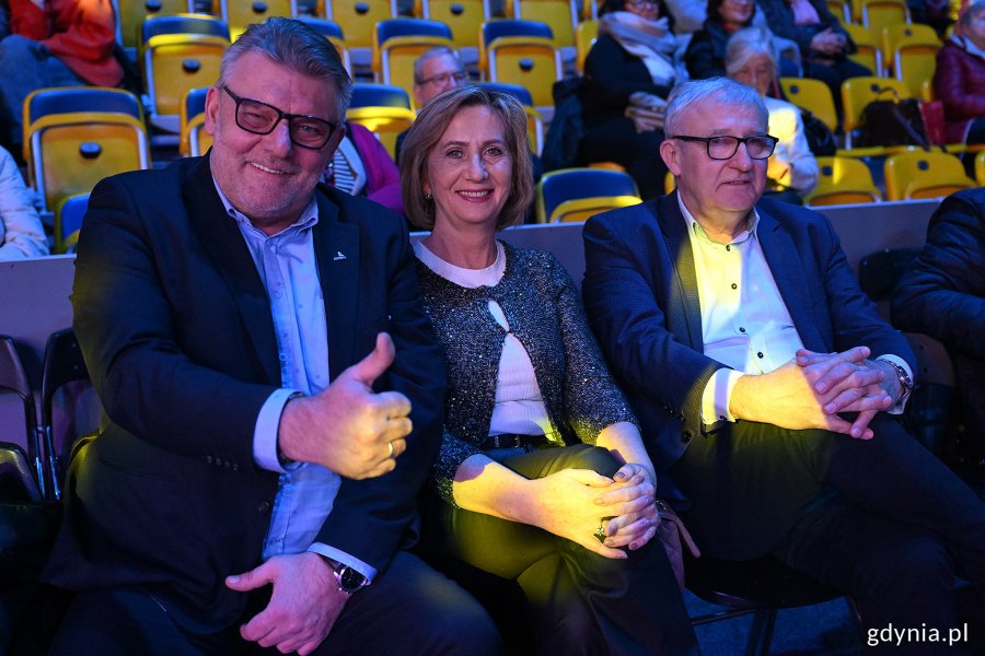 Hala Polsat Plus Arena Gdynia, trybuny, przyciemnione światło, trzy osoby pozują do zdjęcia