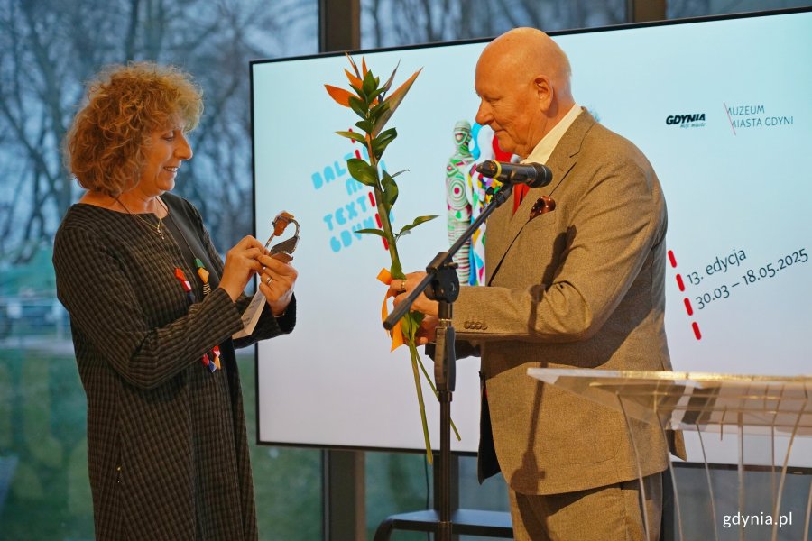 Wojciech Bonisławski w eleganckim garniturze wręczający Nagrodę Marszałka Województwa Pomorskiego i kwiata Caren Garfen
