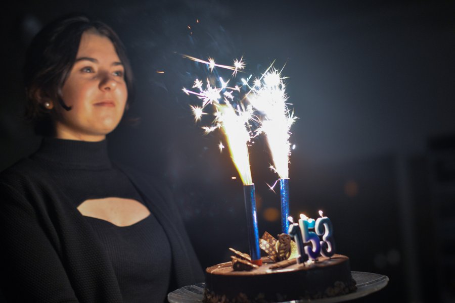 Dziewczyna niosąca tort z płonącymi flarami, na torcie świeczki układające się w cyfrę 153