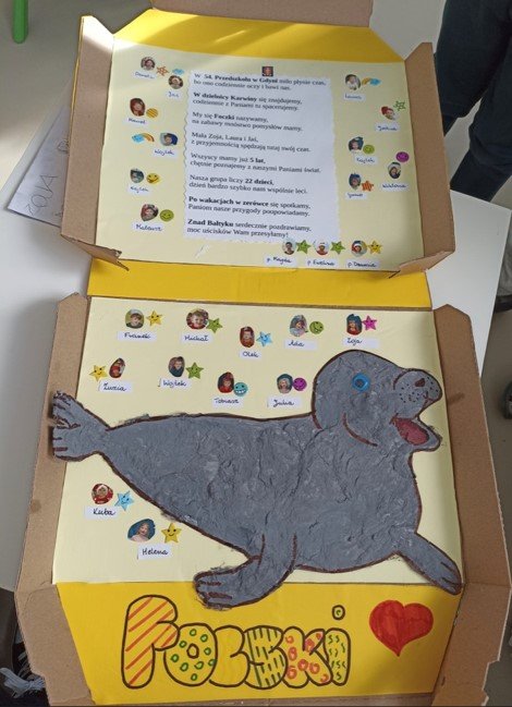 Pudełko od pizzy, w środku rysunek foczki, wiersz i zdjęcia przedszkolaków