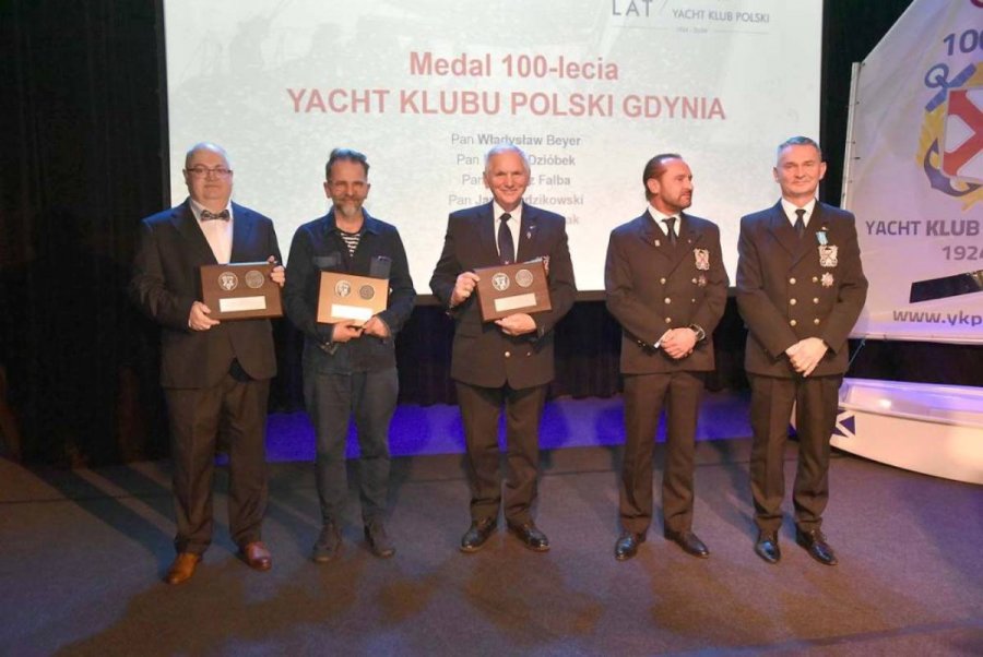 Grupa osób stojących na scenie i mających za plecami biały ekran