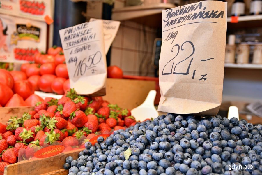 Stoisko z borówkami, truskawkami i pomidorami. U góry, na owocach stoją kartki z nazwami produktów i cenami. W tle pólka ze słoikami // fot. Sławomir Okoń