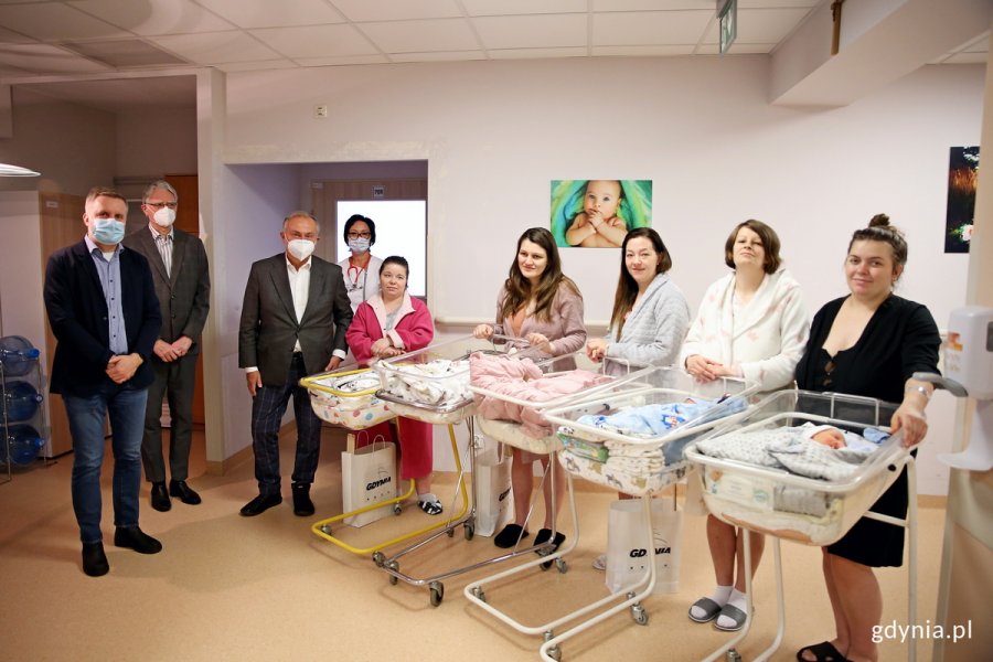 W szpitalu stoi pięc kobiet z noworodkami w wózkach oraz trzech mężczyzn i jedna kobieta.