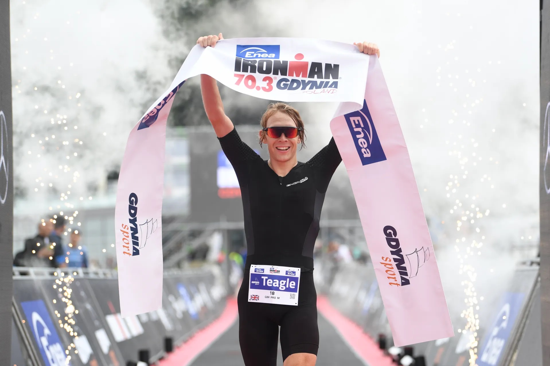 Na zdjęciu widzimy Jamesa Teagle'a, kt&oacute;ry trzyma w g&oacute;rze wstęgę oznaczającą linię mety.