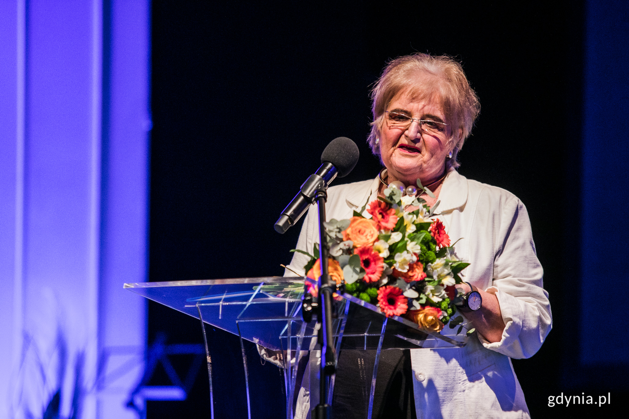 Maria Piradoff-Link, laureatka Medalu im. Eugeniusza Kwiatkowskiego podczas uroczystej sesji Rady Miasta Gdyni. Stoi przy mikrofonie. W rękach trzyma bukiet kwiatów // fot. Karol Stańczak