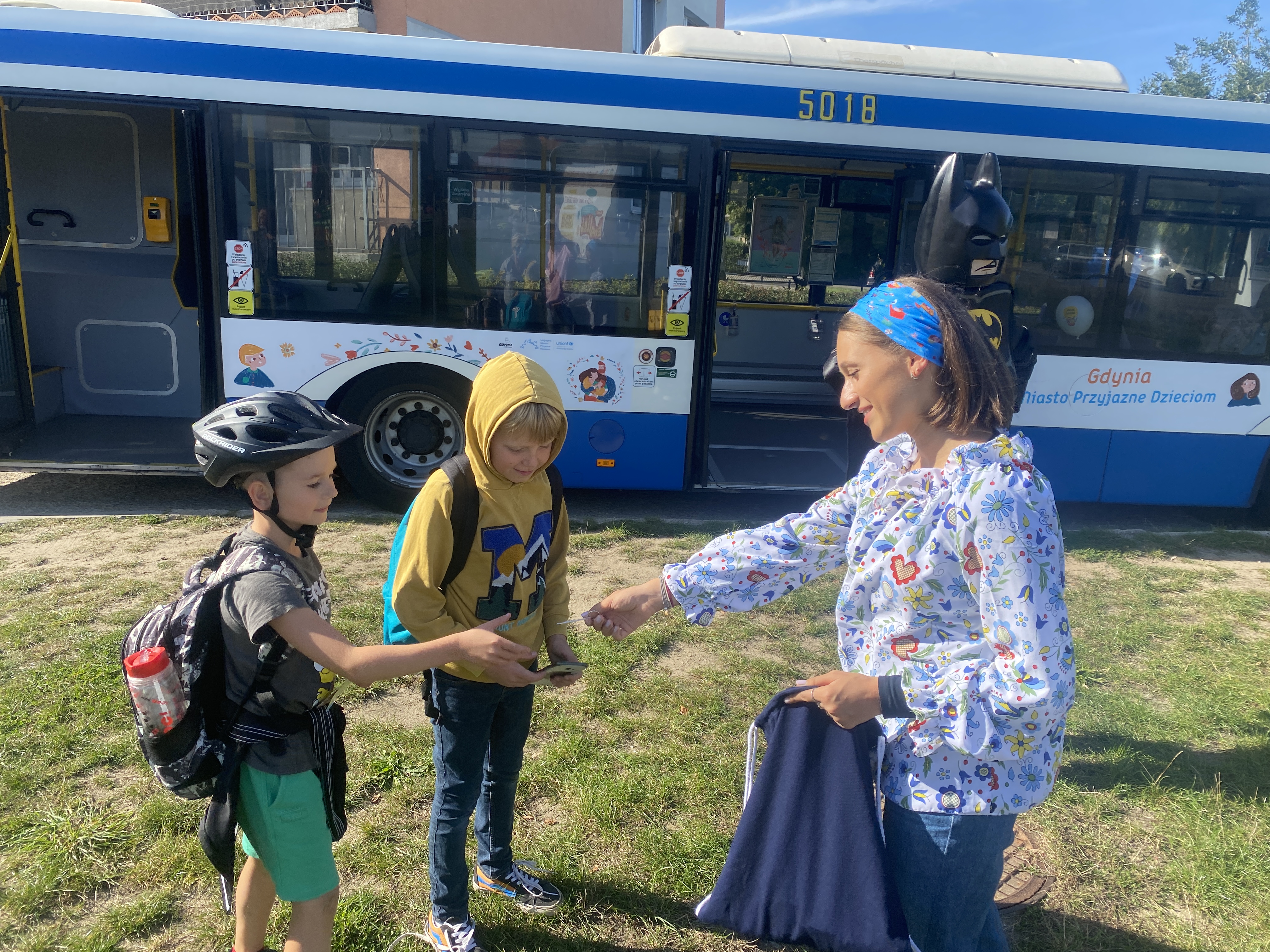 Animatorka rozdaje upominki dzieciom przy autobusie z napisem „Miasto Przyjazne Dzieciom”