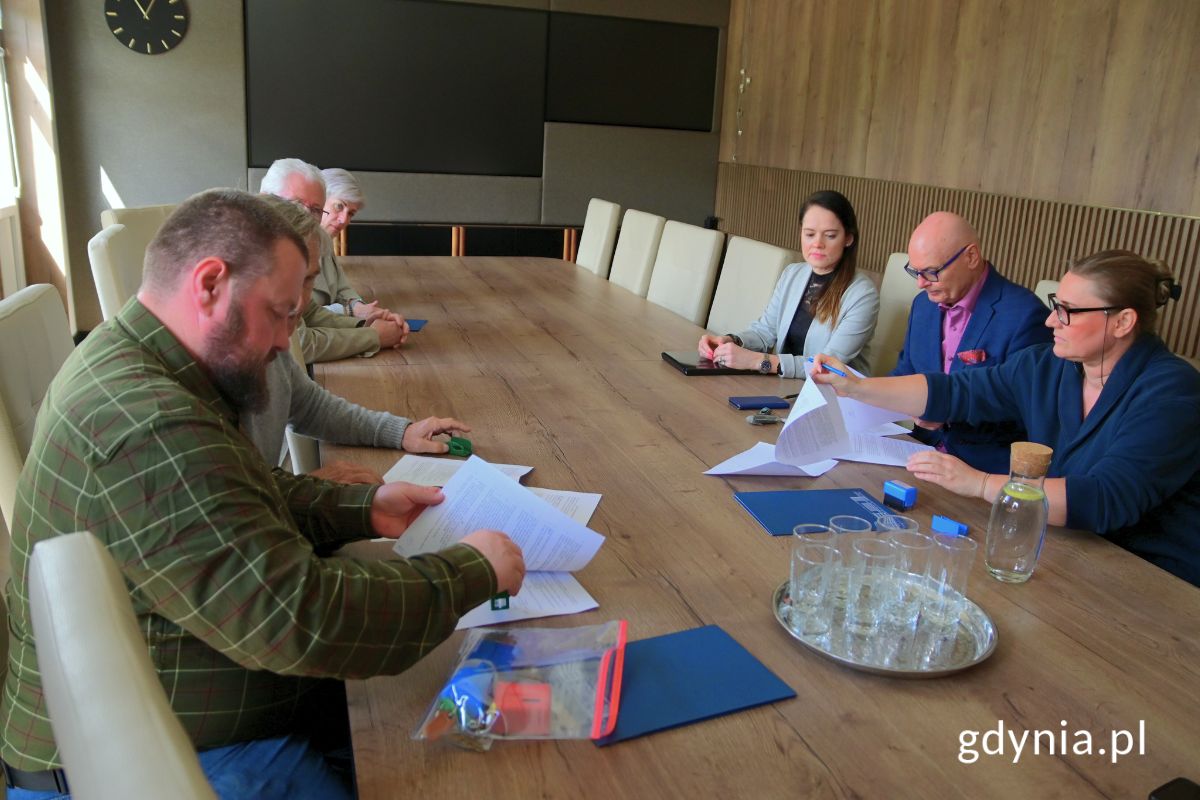 Grupa osób siedzących przy stole konferencyjnym i podpisujących umowy