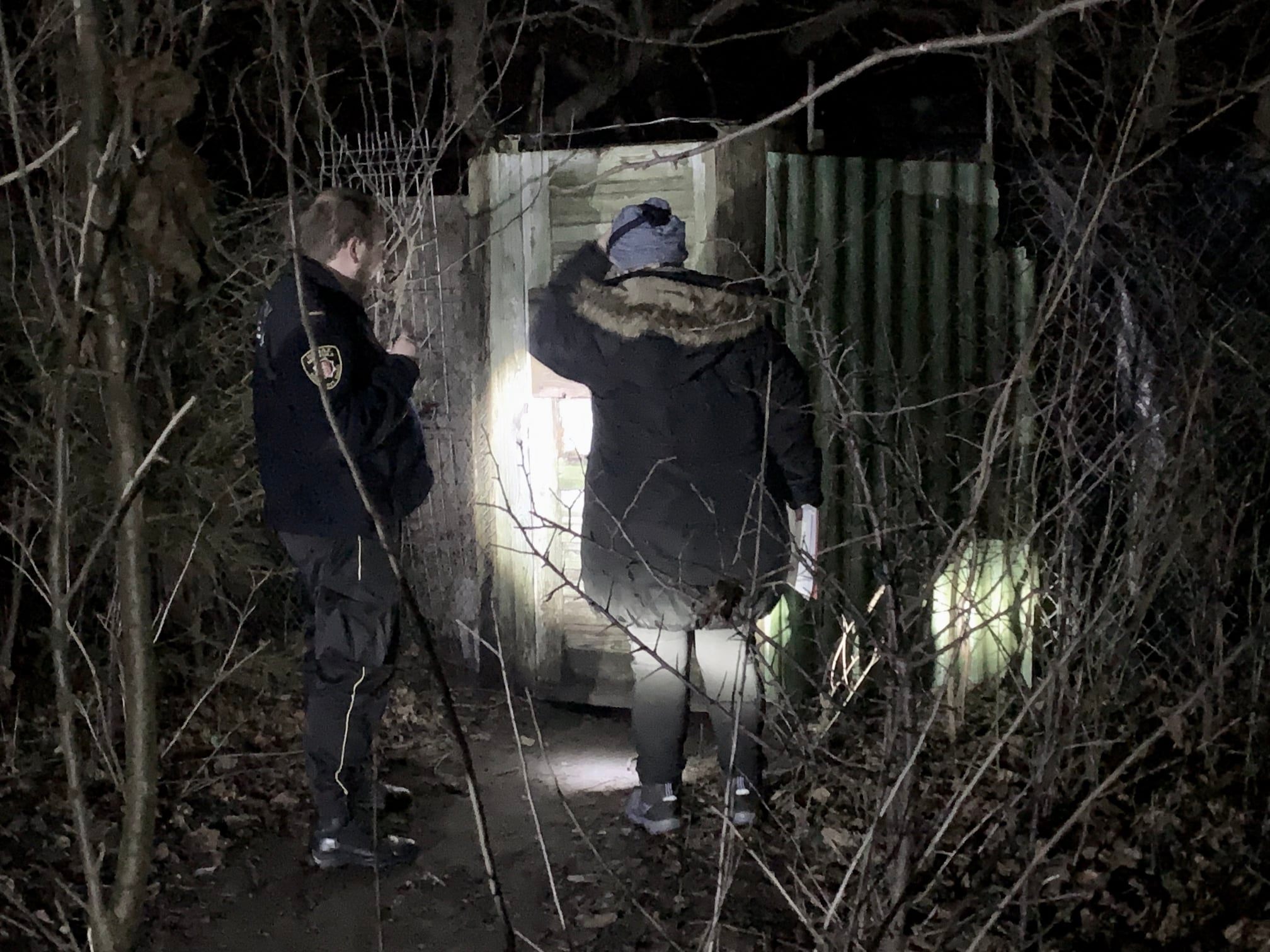 Funkcjonariusze stoją przed szałasem-szopą zamieszkiwanym przez bezdomnego