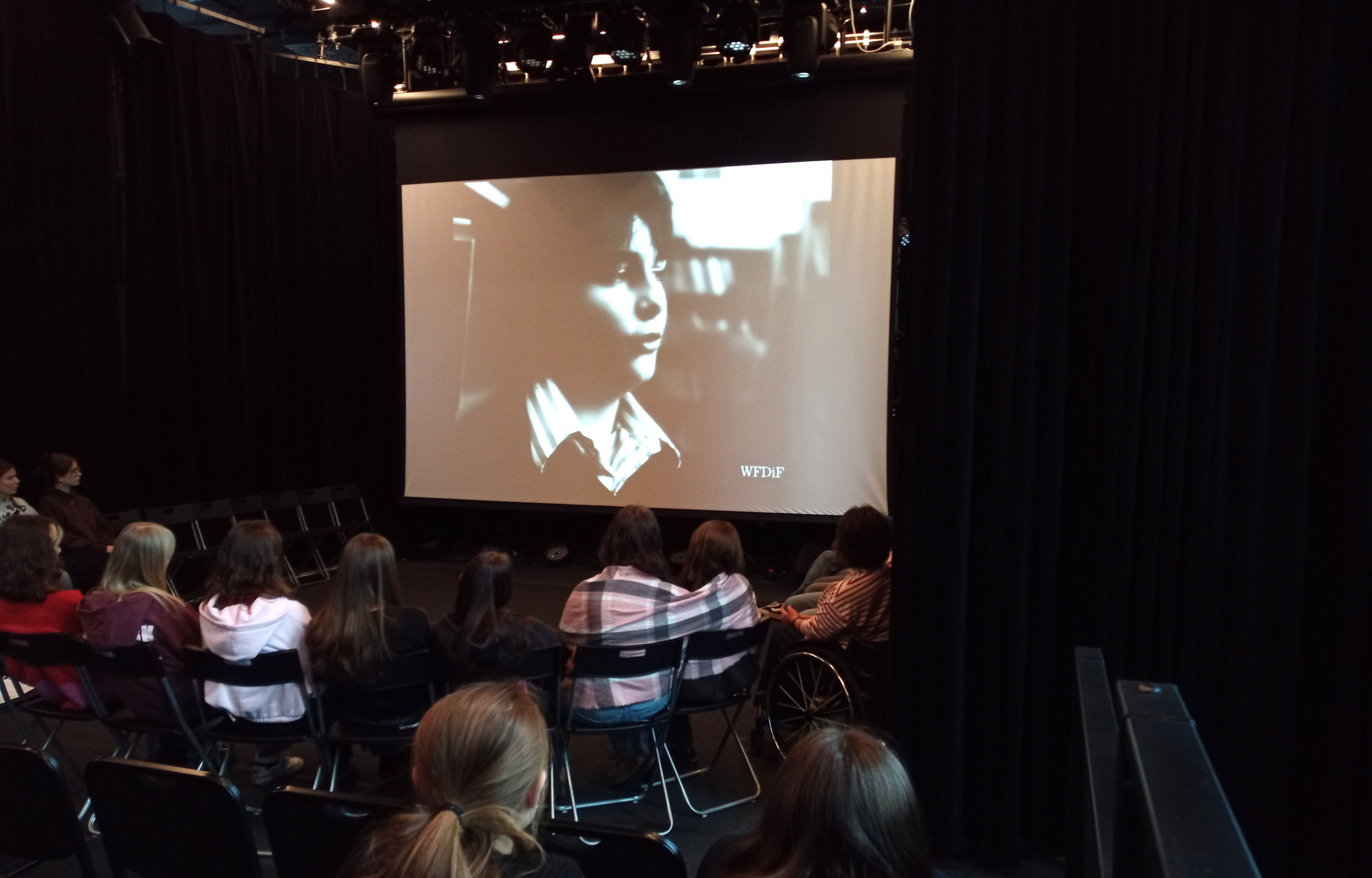 Młodzież siedząca tyłem przed dużym ekranem na warsztatach kina dokumentalnego w Konsulacie Kultury