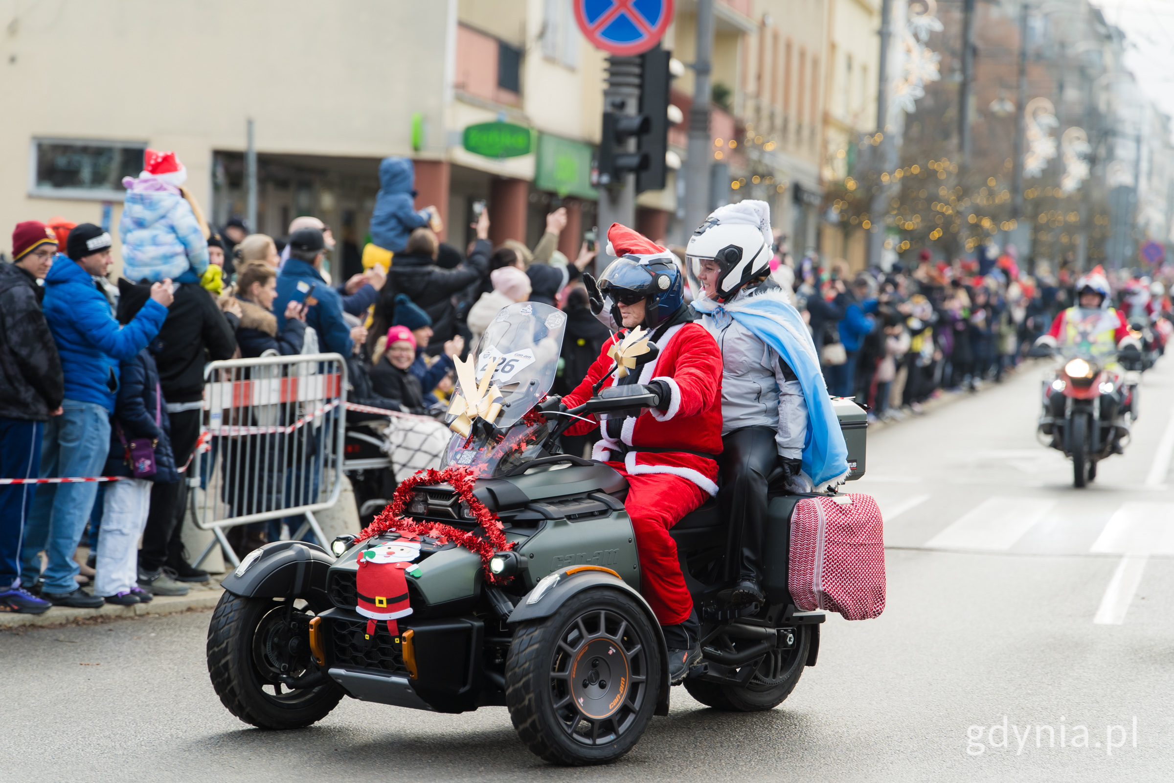 Ulica Świętojańska, parada mikołaj&oacute;w na motocyklach, na tr&oacute;jkołowcu jedzie motocyklista w przebraniu mikołaja i prezydent Gdyni w niebieskim stroju