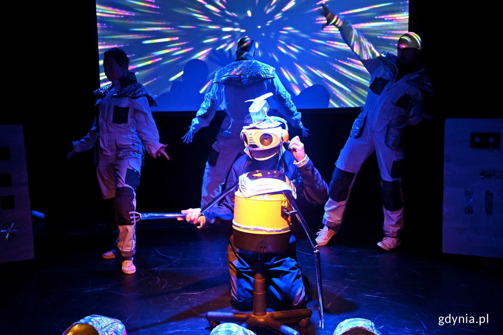 Zdjęcie z próby spektaklu „Dlaczego nie lecimy do gwiazd?” w Teatrze Gdynia Główna. Na pierwszym planie robot STASIU, w tle astronauci i animacje przestrzeni kosmicznej // fot. Magdalena Czernek