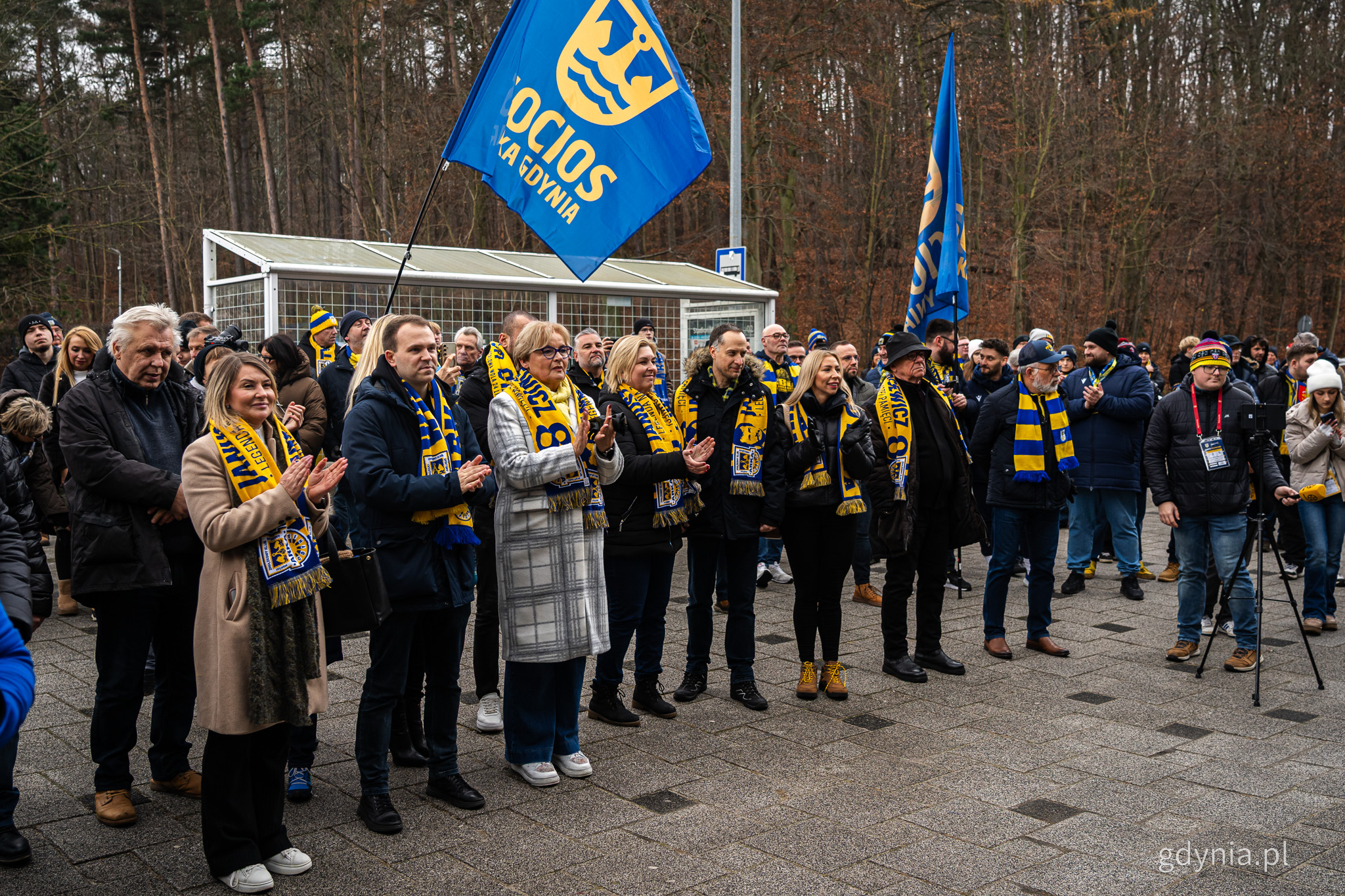 Plac przed Stadionem Miejskim, grupa os&oacute;b bije brawo, widoczne flagi kibic&oacute;w Arki Gdynia