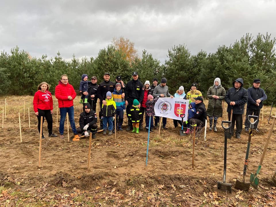 Na zdjęciu widzimy uczestnik&oacute;w jubileuszu stojących w rzędzie na polu zasadzonych drzew