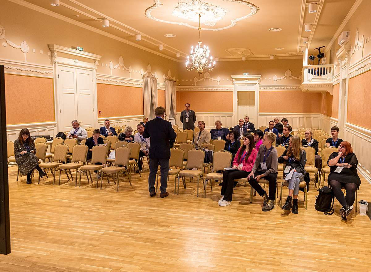 Ludzie siedza na krzesłach w sali.