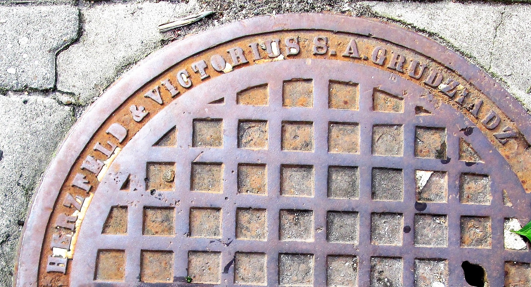 Żeliwna pokrywa studzienki kanalizacyjnej z firmy &bdquo;Herzfeld i Victorius&rdquo; z Grudziądza, występująca w wielu miejscach miasta (detal)