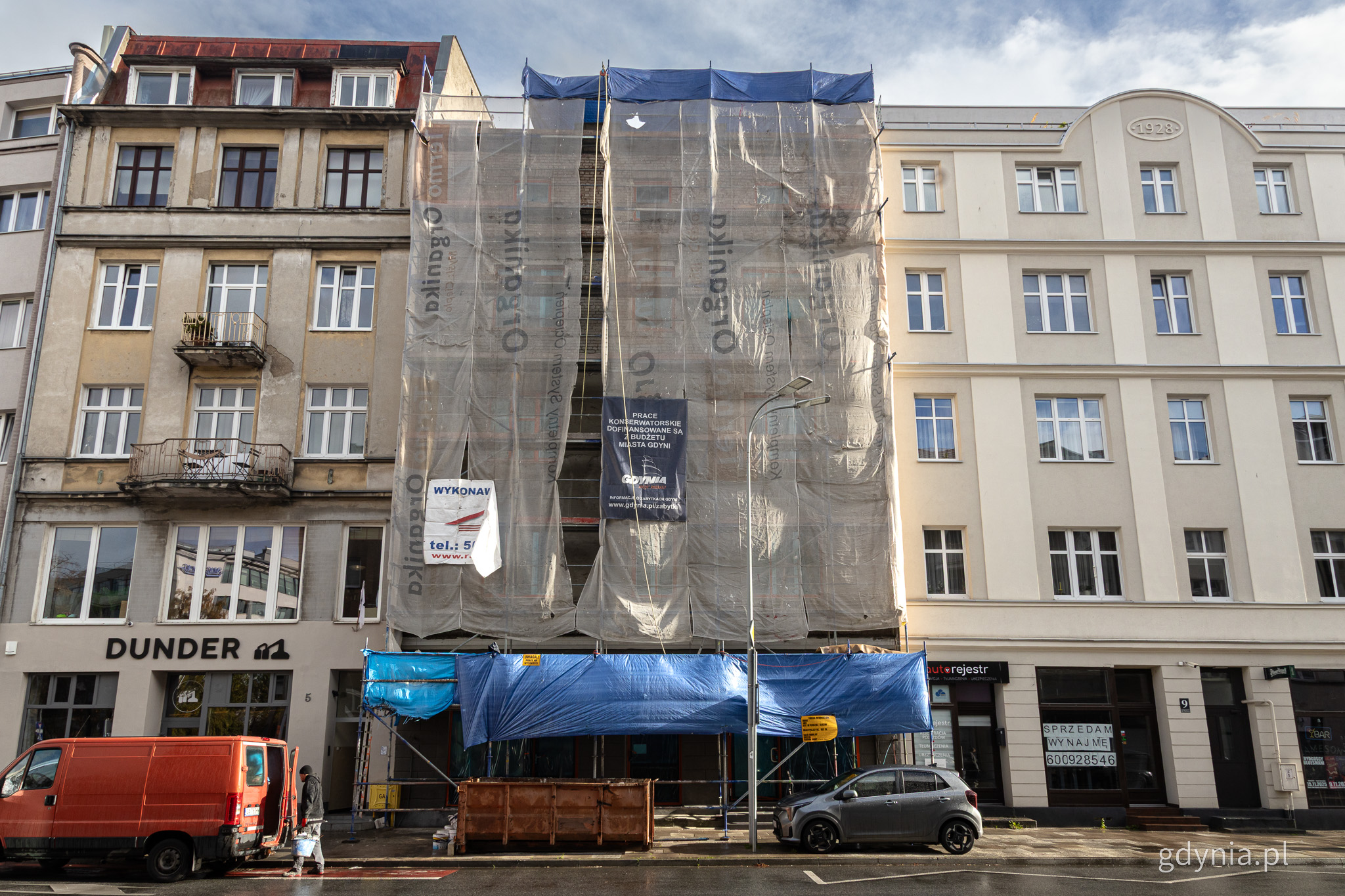 Kamienice przy ulicy Portowej, elewacje, rusztowania, kontener na odpady, zaparkowane samochody, fragment jezdni