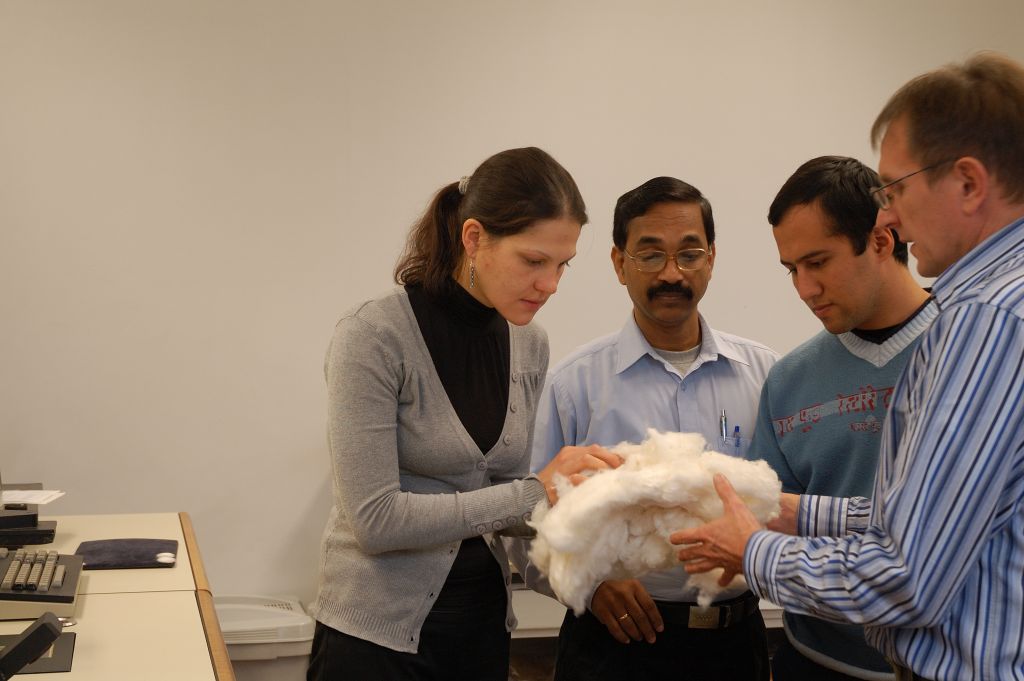 Grupa os&oacute;b w sali, mężczyzna trzyma kłęb bawełny, obok kobieta, kt&oacute;ra dotyka materiału