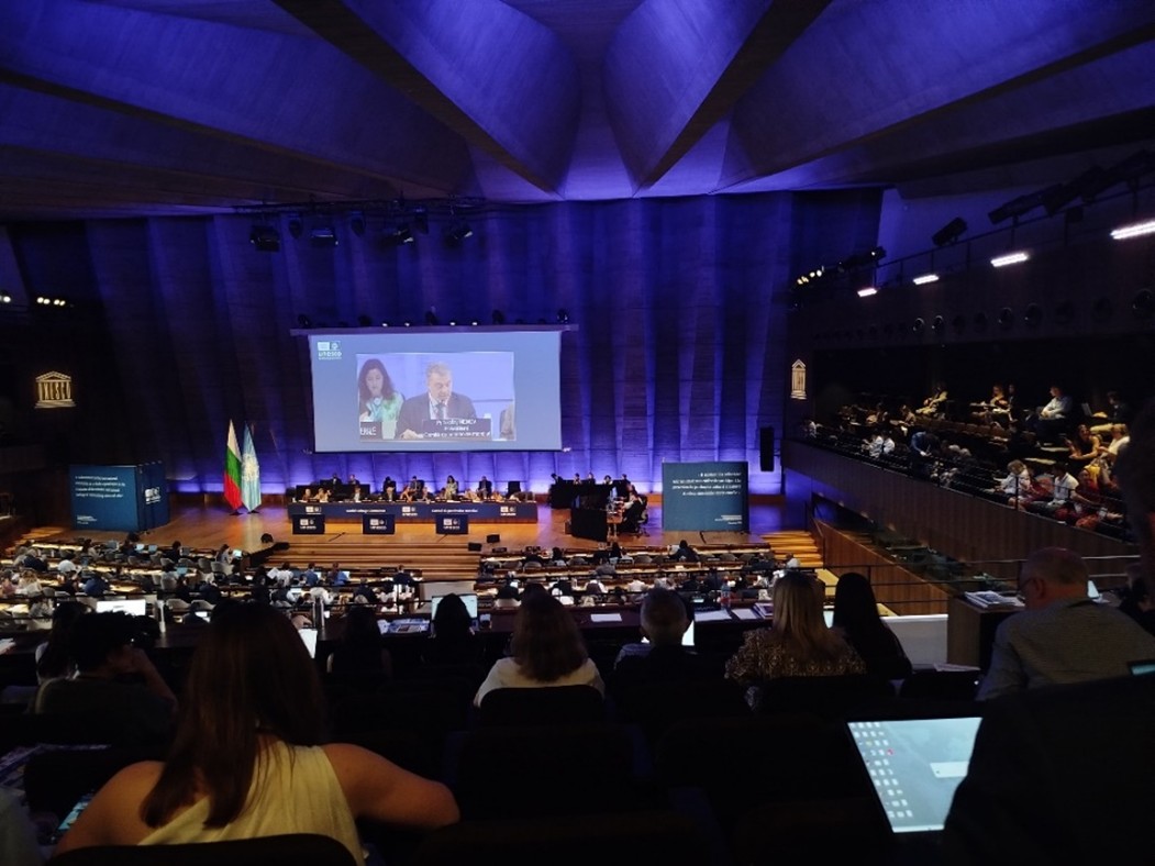 Sala konferencyjna, niebieskie światło, tłum ludzi na widowni, na ektanie wyświetlana prezentacja