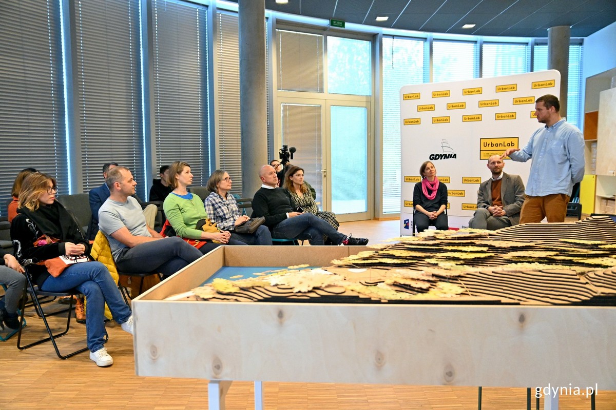 Mężczyzna przemawia na sali do grupy siedzących os&oacute;b.