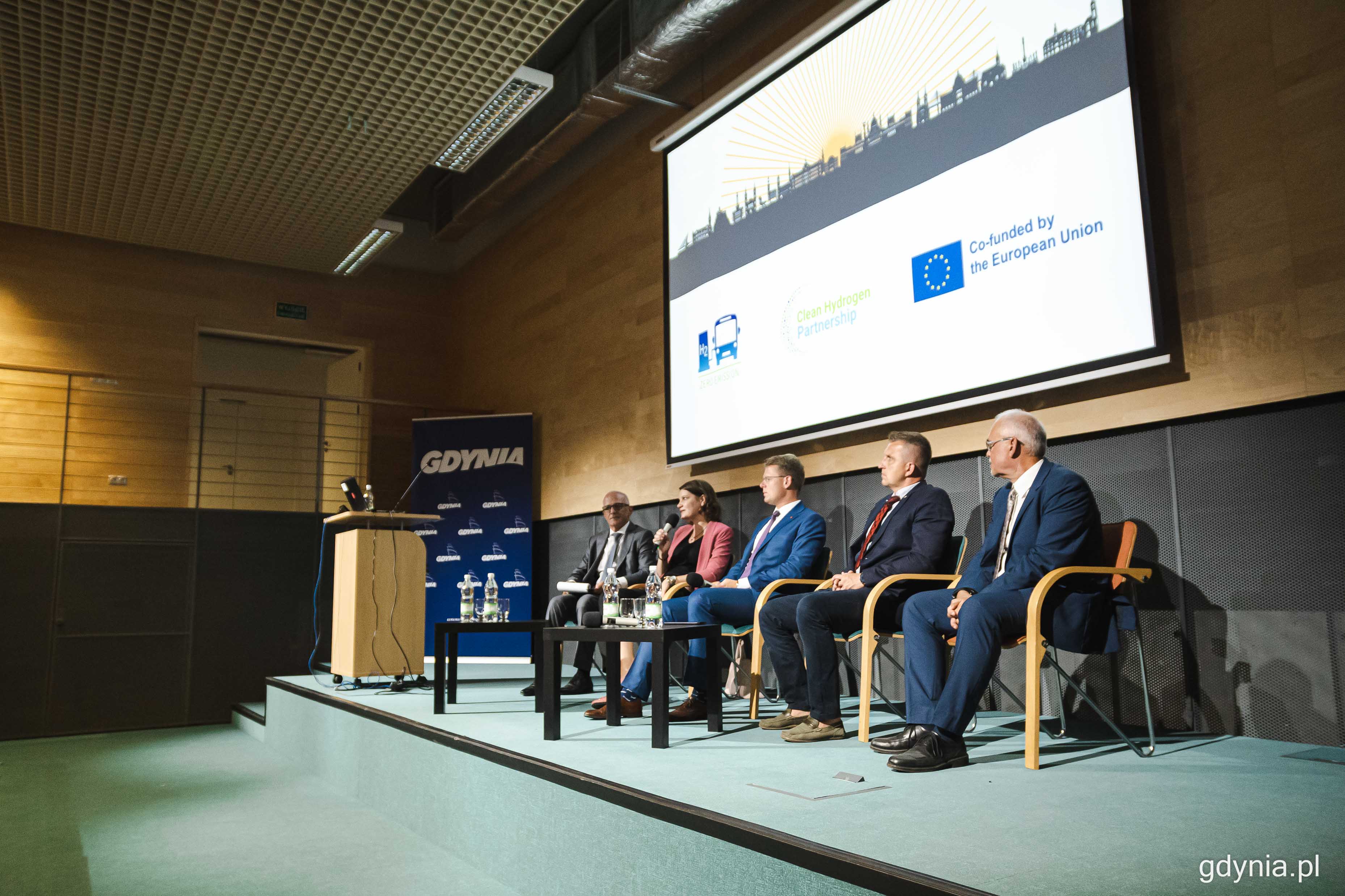 Sala Morska w PPNT Gdynia, prezentacja na wyświetlaczu, na scenie siedzi pięć os&oacute;b obok siebie, przemawia przez mikrofon Katarzyna Gruszecka-Spychała