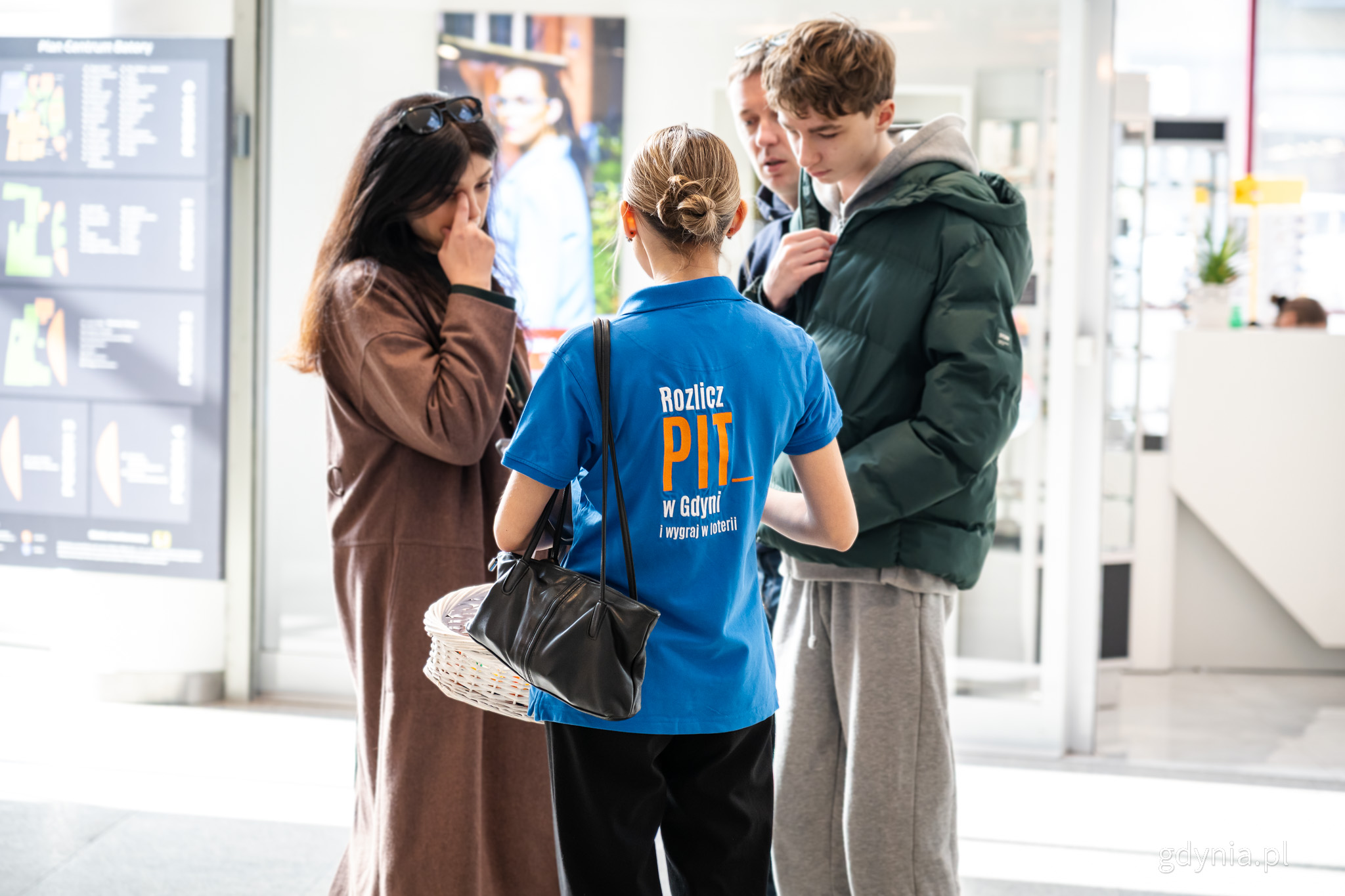Hol Centrum Batory, kobieta z napisem Rozlicz PIT w Gdyni udziela informacji trzyosobowej grupie