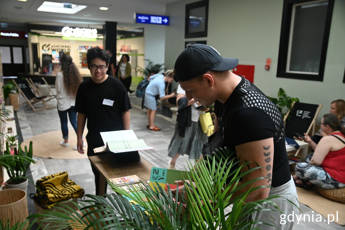 Strefa czytelnictwa na dworcu PKP Gdynia, przy stoisku z książkami rozmawia dw&oacute;ch pan&oacute;w 