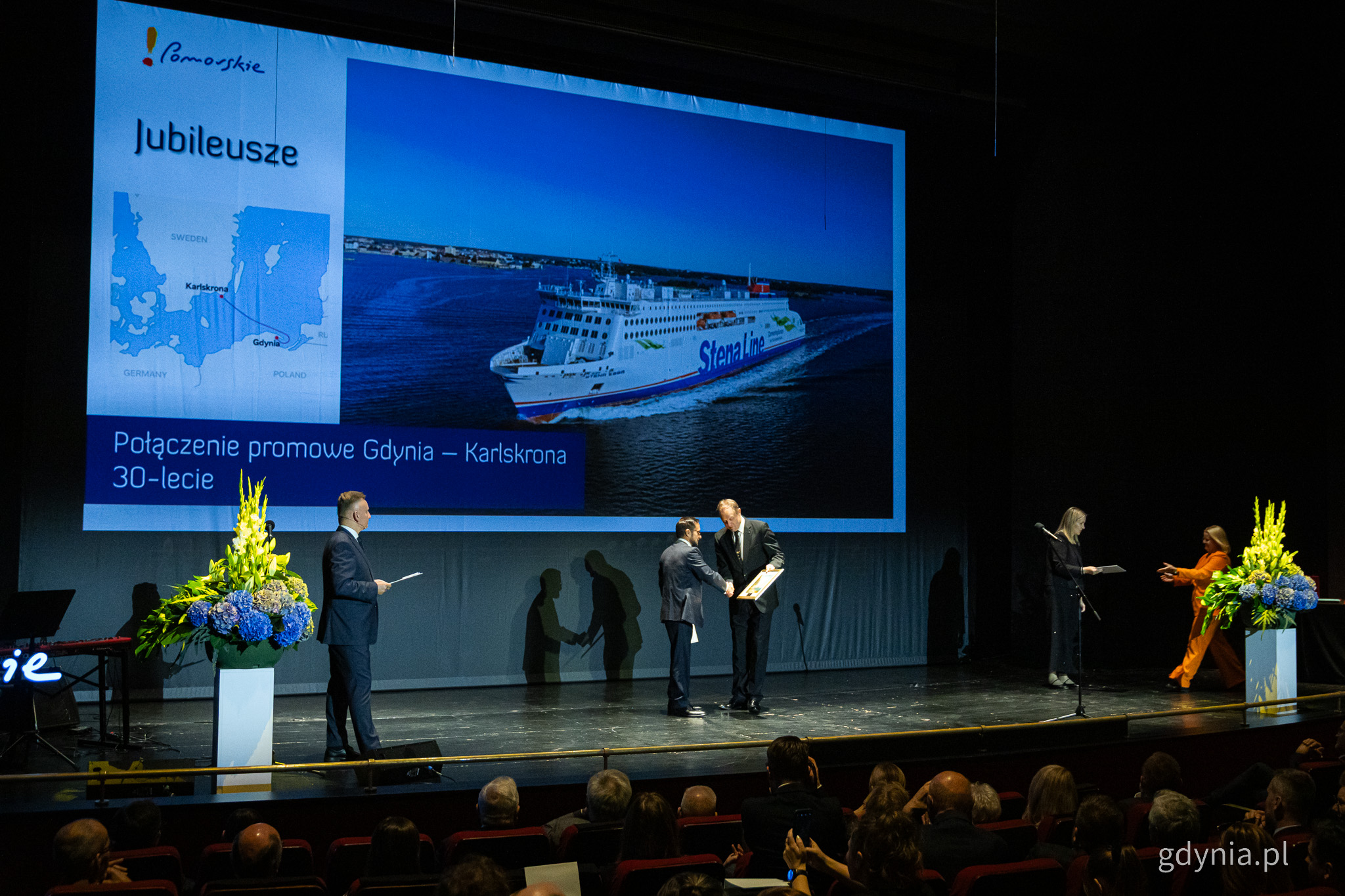 Scena opery, trzy osoby, wręczenie nagrody, na ekranie zdjęcie promu Stena Line