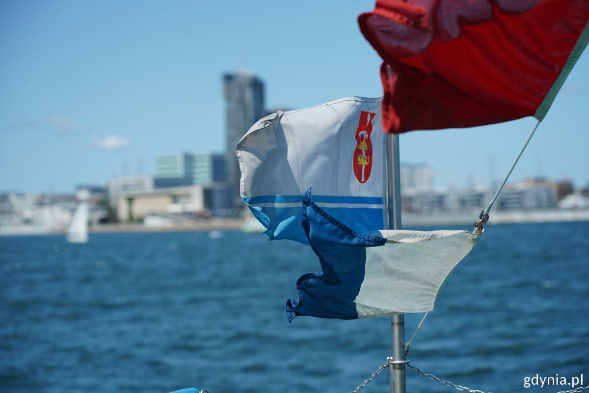 Flaga z herbem Gdyni na tle plaży Śr&oacute;dmieście