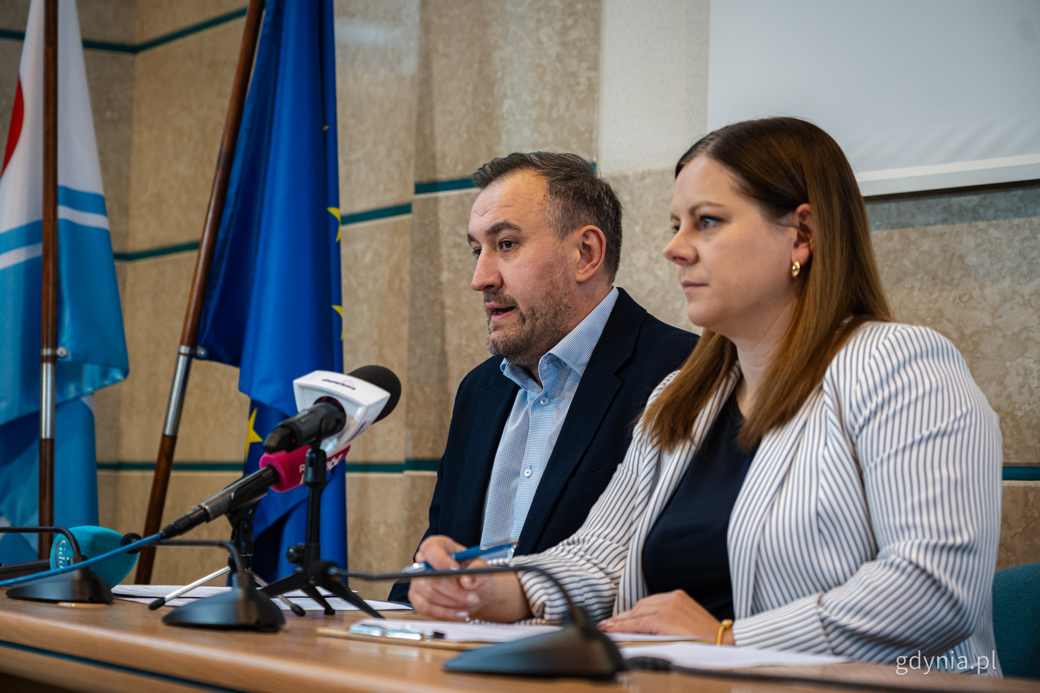 Sala obrad Rady Miasta w Urzędzie Miasta Gdyni, przy stole siedzą Aleksandra Kosiorek i Tomasz Augustyniak, przemawiają do mikrofonu