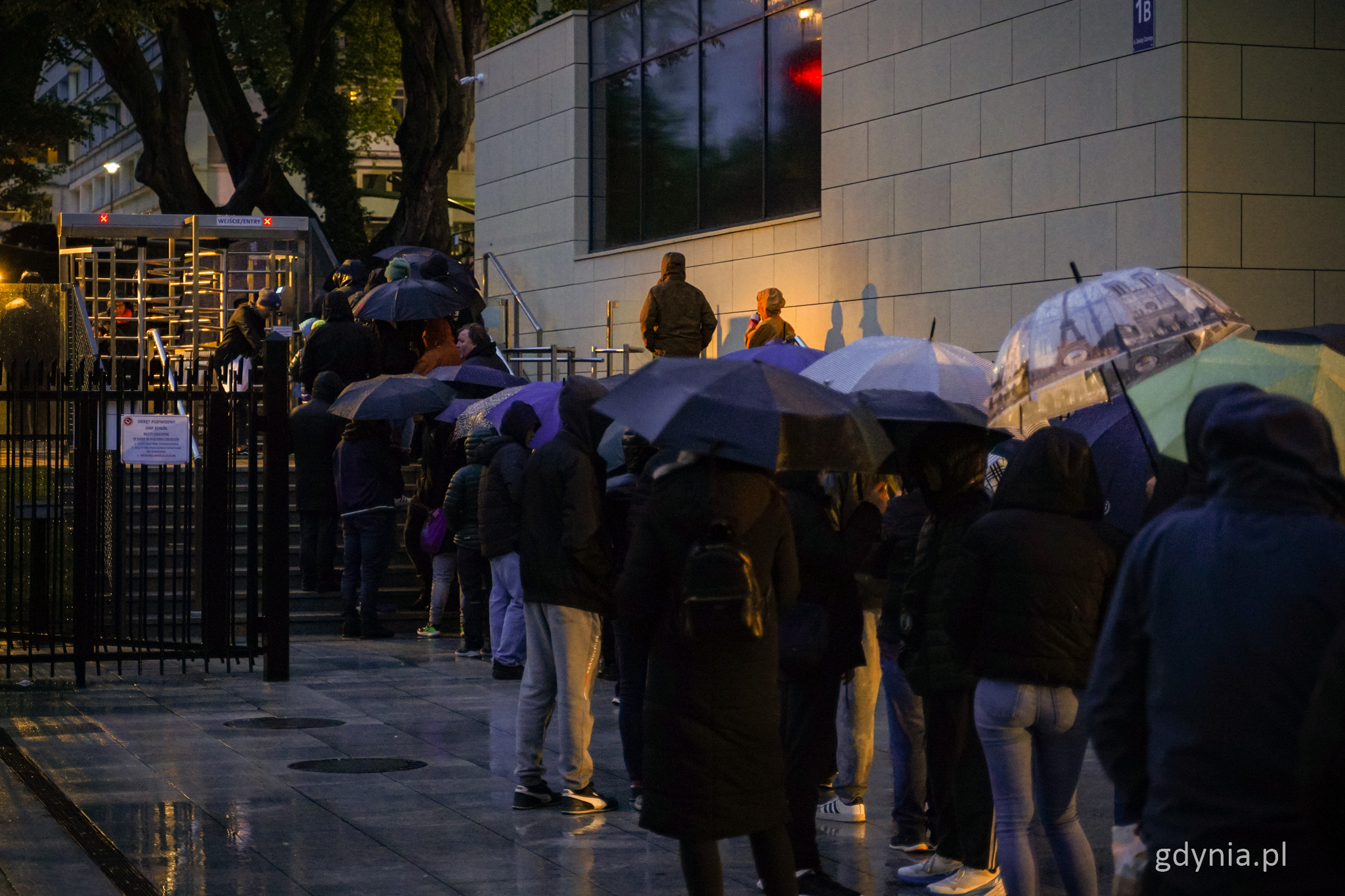 Plac przed Muzeum Marynarki Wojennej, noc, deszcz, kolejka ludzi z parasolami do wejścia