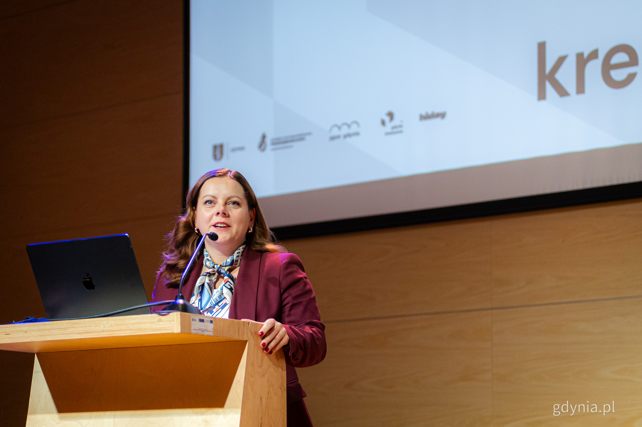 Sala konferencyjna PPNT Gdynia, przy m&oacute;wnicy przemawia Aleksandra Kosiorek, w tle ekran z prezentacją