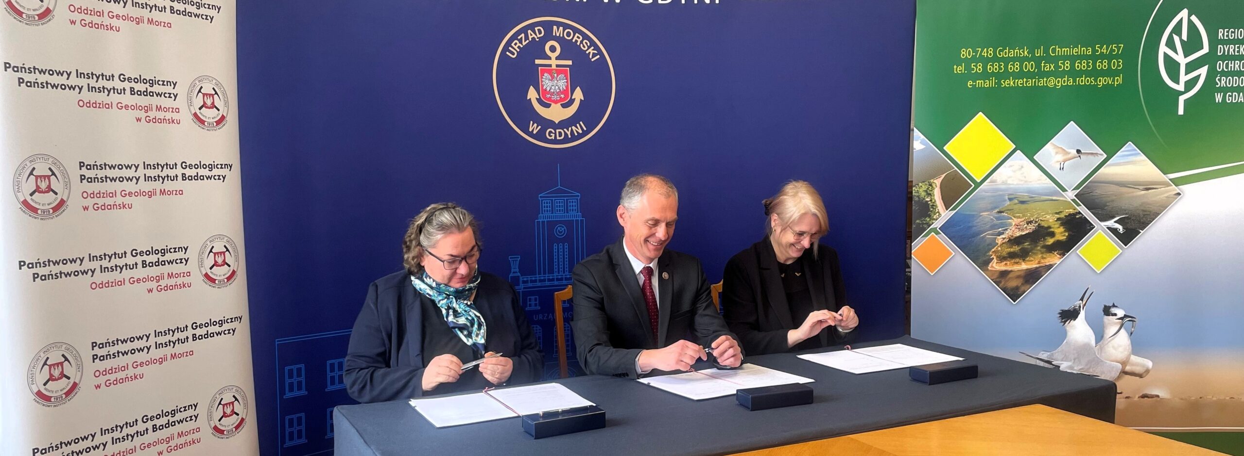 Sala w Urzędzie Morskim, kilka os&oacute;b siedzi przy stole, podpisują dokumenty