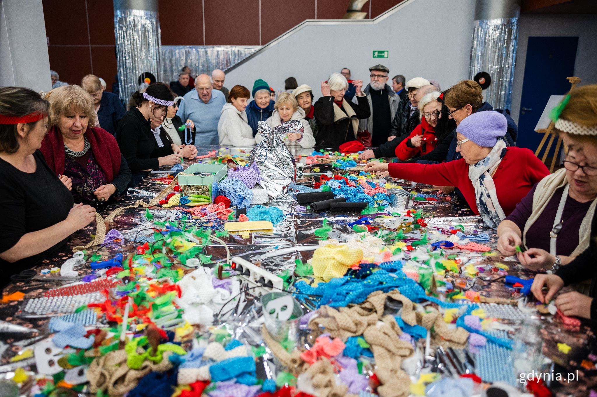 Uczestnicy warsztat&oacute;w kreatywnych w klimacie lat 70. i 80. zorganizowanych z okazji 98. urodzin Gdyni w Polsat Plus Arenie Gdynia stoją przy stole z kolorowymi opaskami, pi&oacute;rami i innymi akcesoriami 