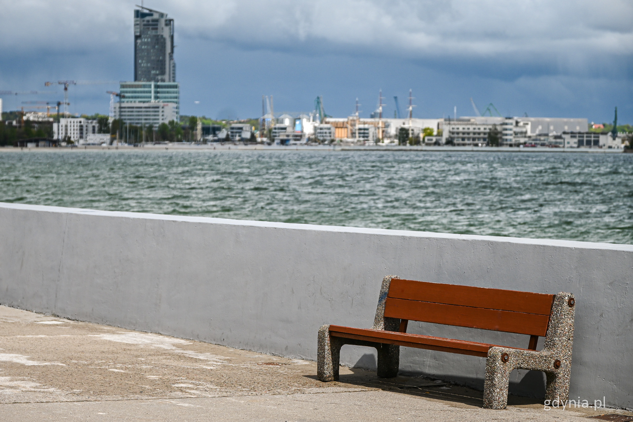 Bulwar Nadmorski, szary murek, ławka, morze, w tle Sea Towers i inne budynki
