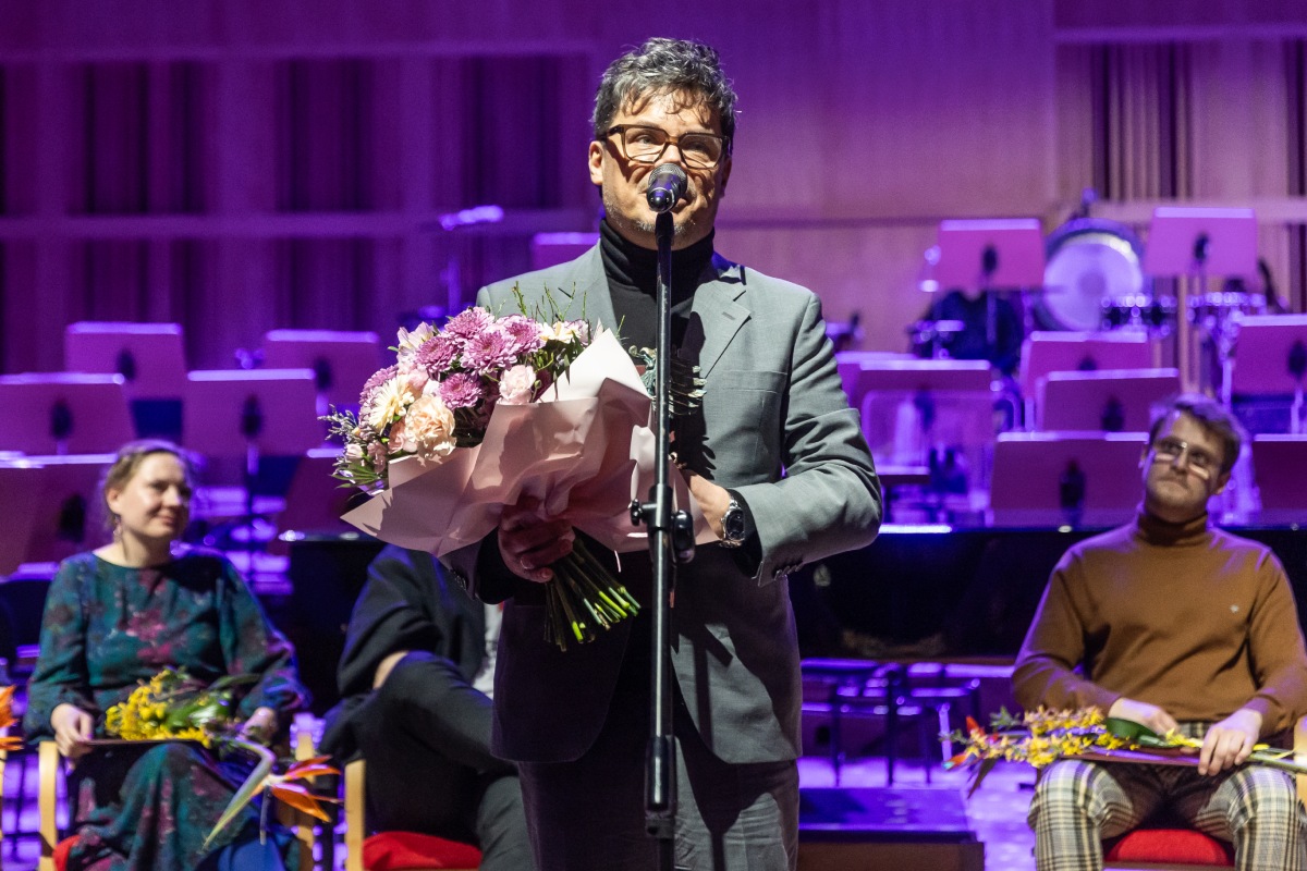 Scenograf Mariusz Napierała podczas gali Pomorskiej Nagrody Artystycznej. Stoi przy mikrofonie, a w rękach trzyma bukiet kwiat&oacute;w i statuetkę gryfa (fot. Piotr Żagiell)