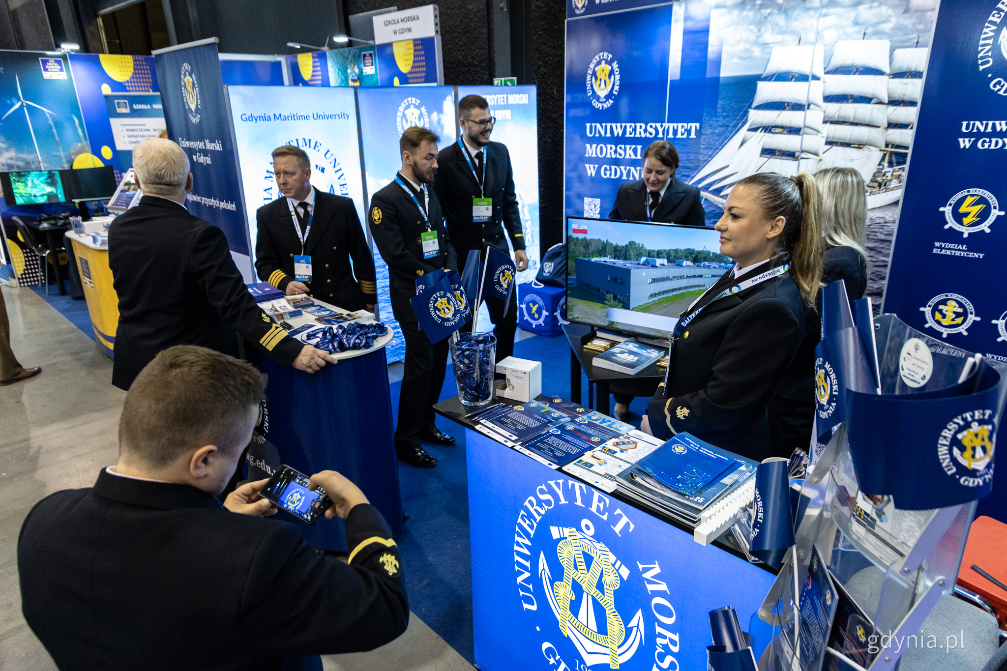 Hala wystawiennicza AmberExpo, stoisko Uniwersytetu Morskiego, kilka os&oacute;b w mundurach uczelni
