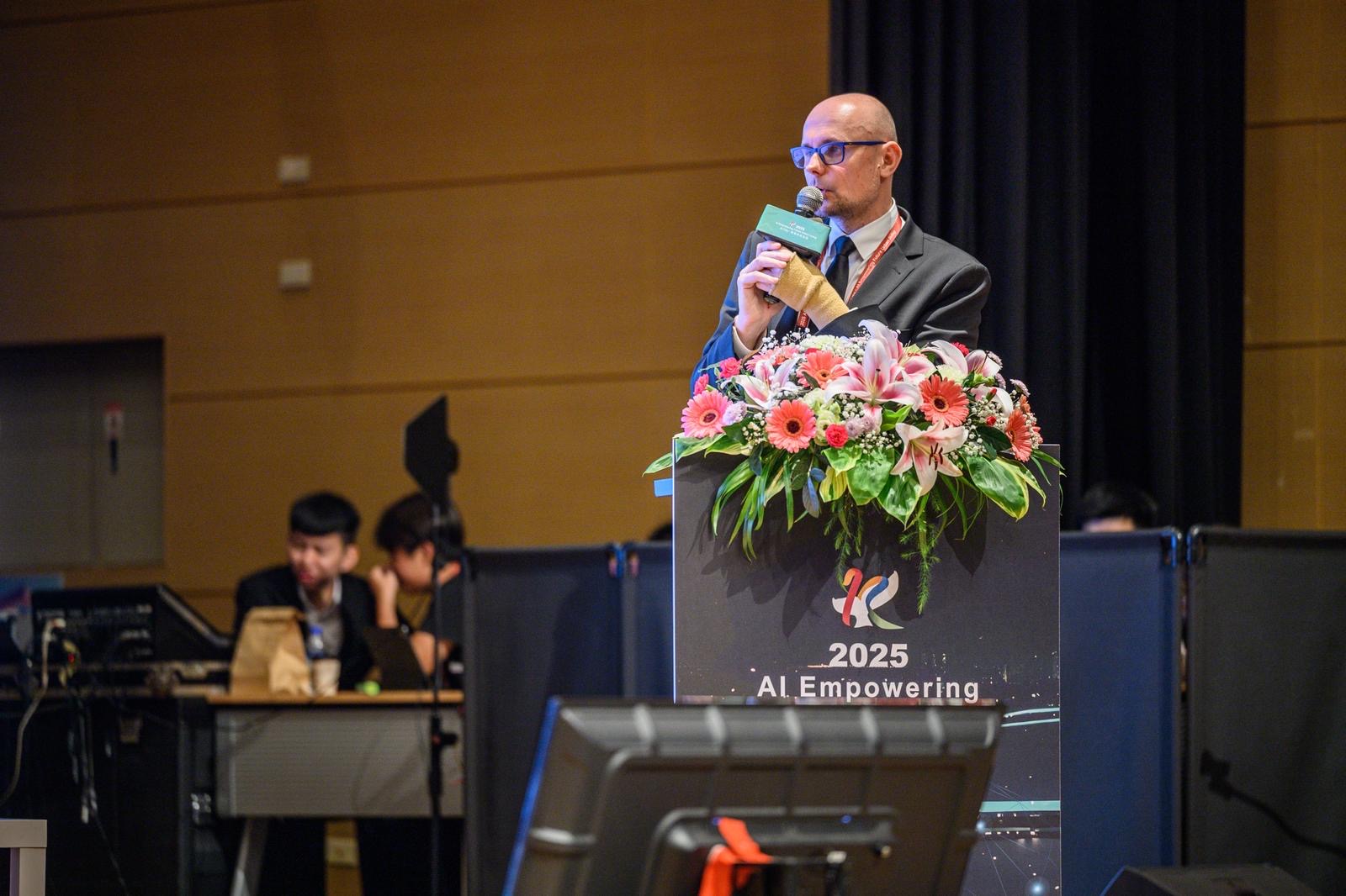 Sala konferencyjna, m&oacute;wnica, Bartłomiej Austen trzyma mikrofon i przemawia