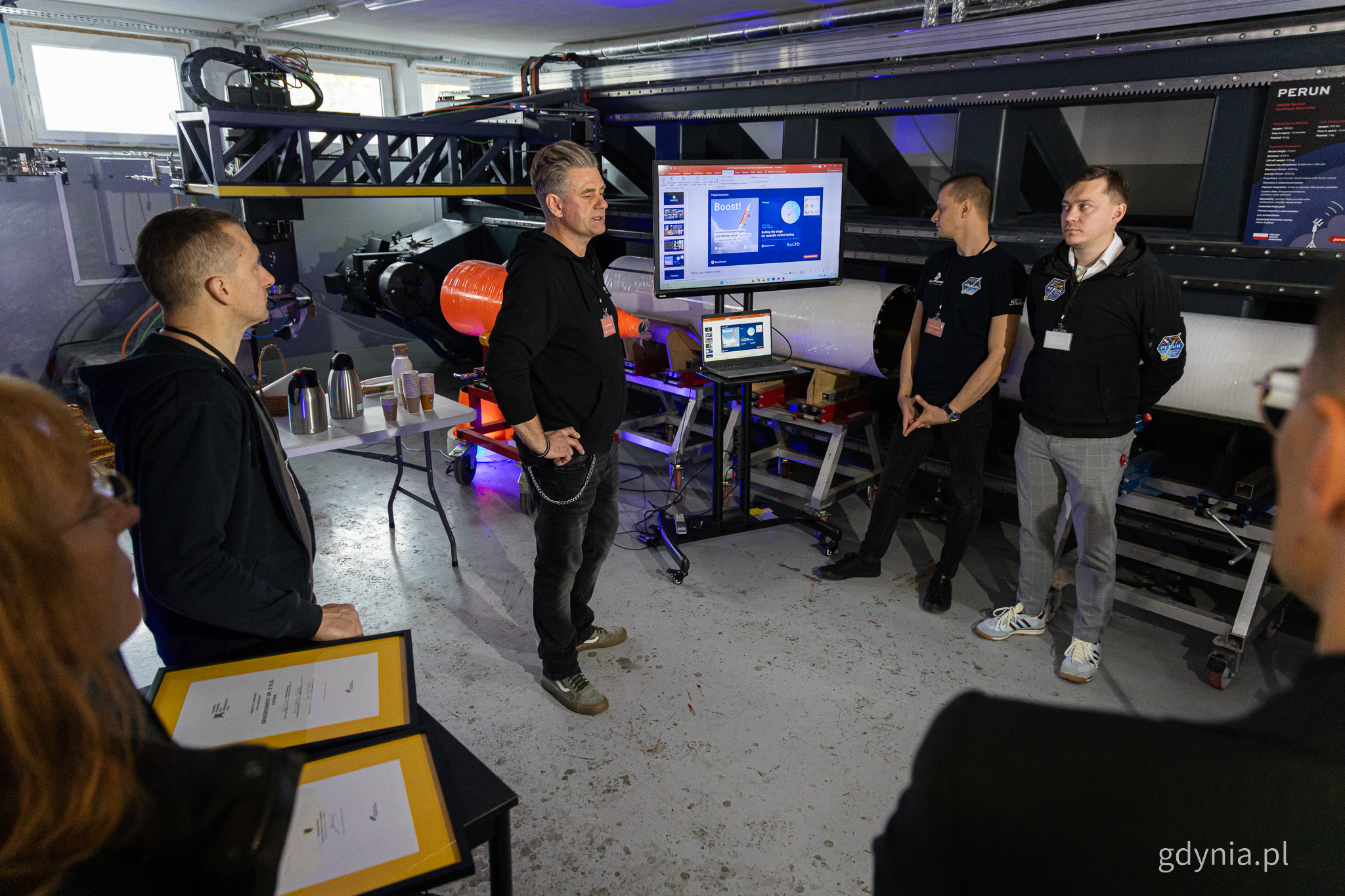 Hala produkcyjna, kilka os&oacute;b przy monitorze, przysłuchująca się grupa ludzi