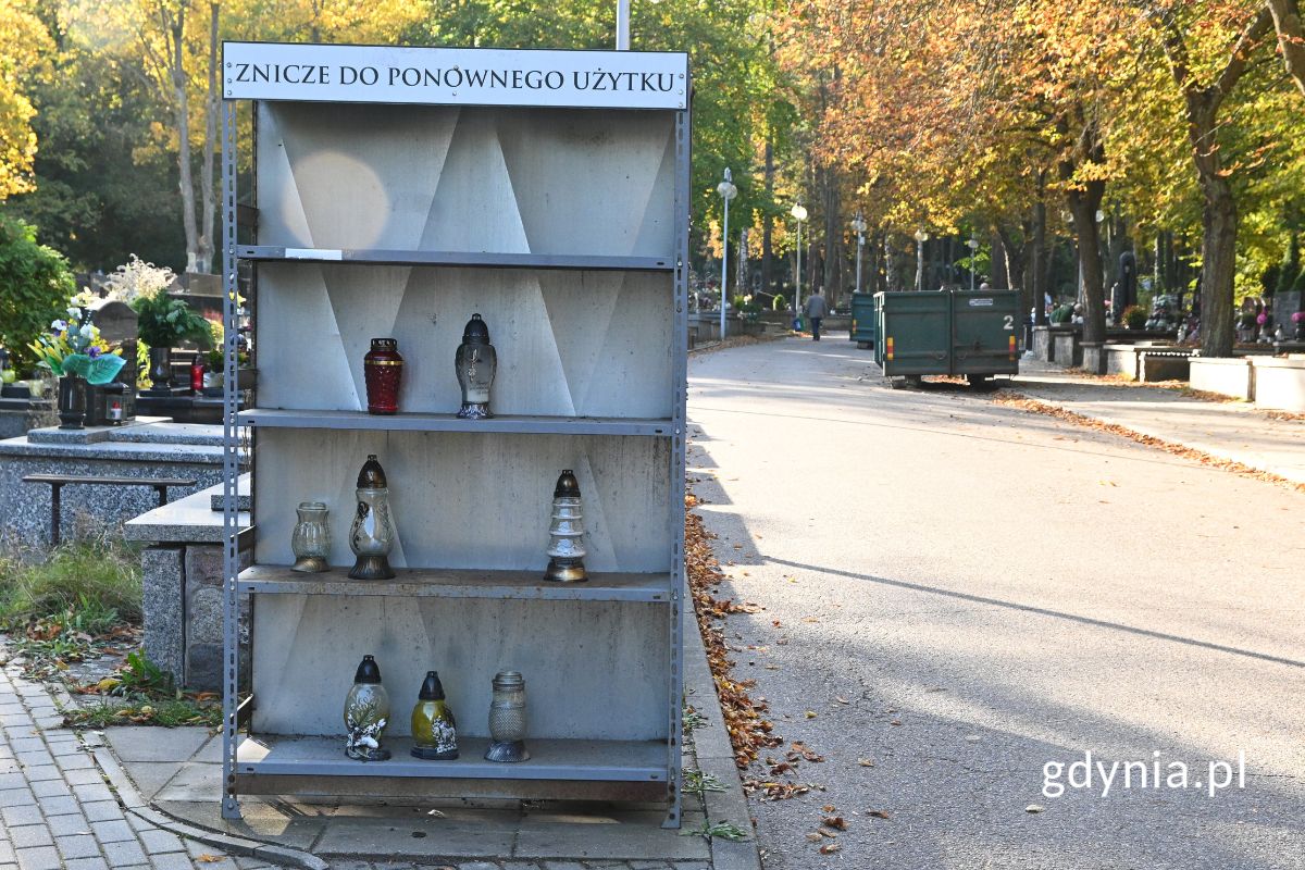 Szary regał na znicze do ponownego użytku na tle cmentarza