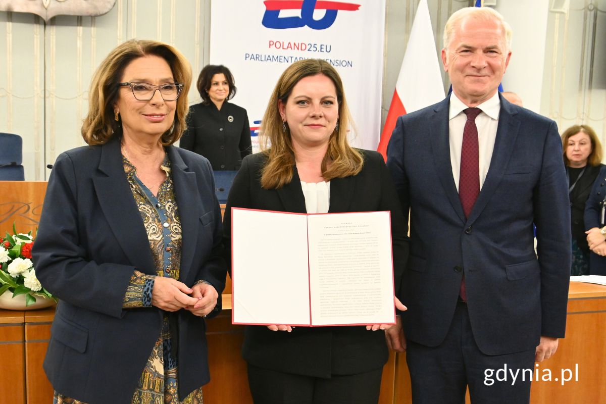 Marszałek Senatu Małgorzata Kidawa-Błońska, prezydent Gdyni Aleksandra Kosiorek i senator Sławomir Rybicki stojący w sali posiedzeń Senatu z egzemplarzem uchwały