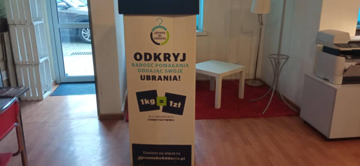 Biało-niebieski kartonowy pojemnik na odzież stojący w korytarzu biblioteki