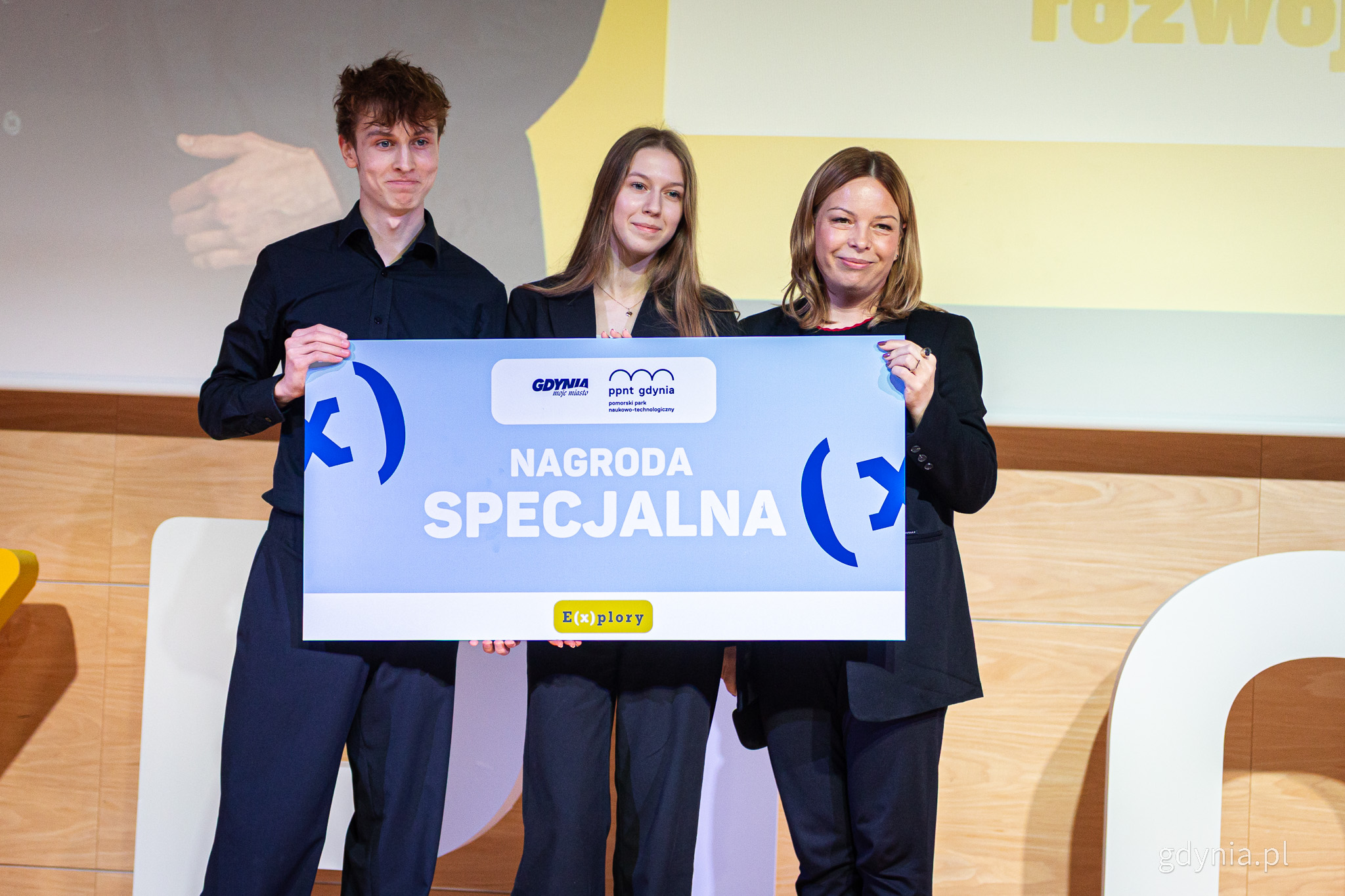 Scena PPNT Gdynia, do zdjęcia pozują Tomasz Gerka, Laura Grafińska i Oktawia Gorzeńska, trzymają planszę z nazwą nagrody