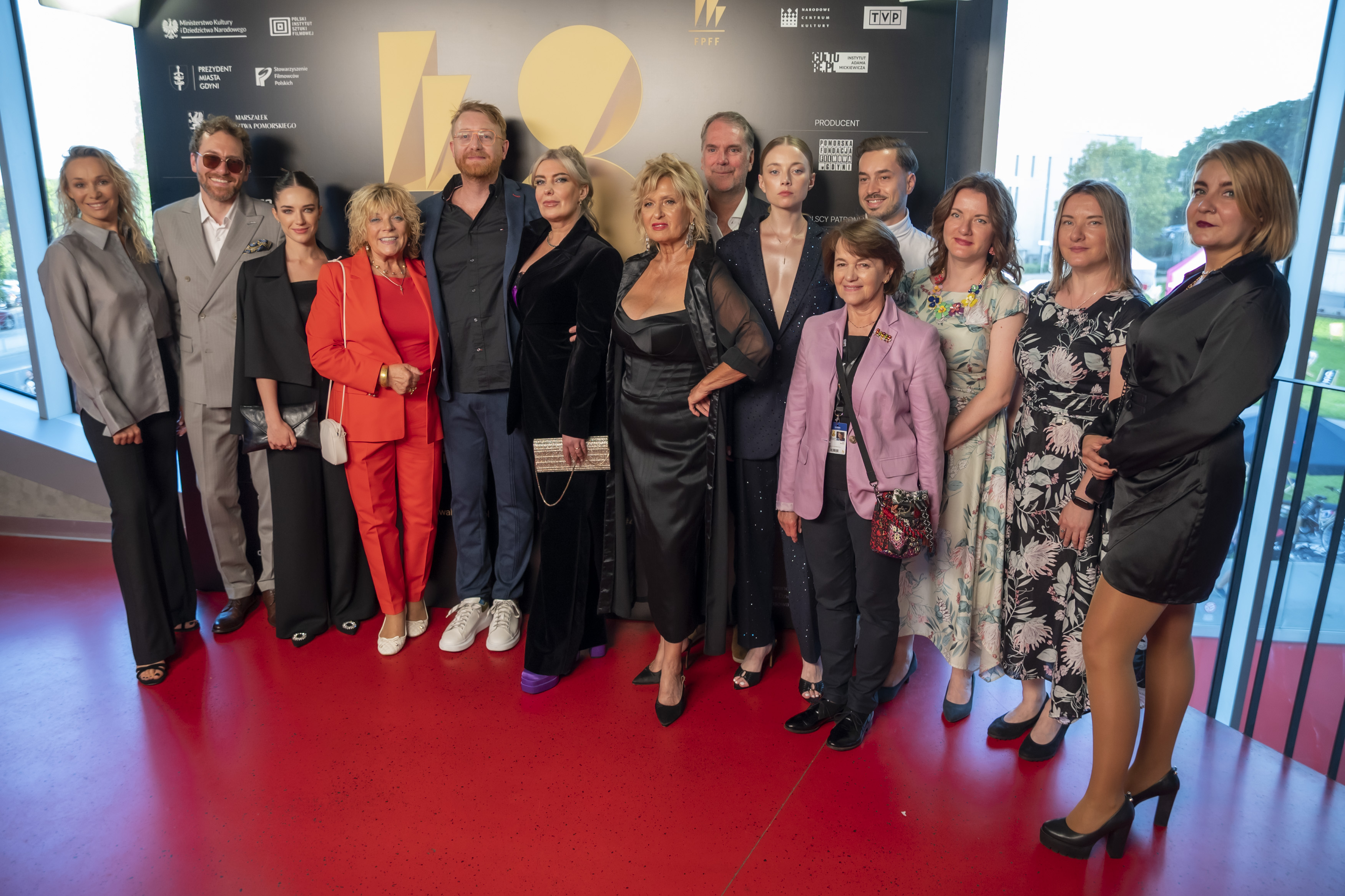 Ścianka FPFF, grupa os&oacute;b - filmowc&oacute;w - pozuje do zdjęcia, czerwona podłoga, przestrzenie Gdyńskiego Centrum Filmowego